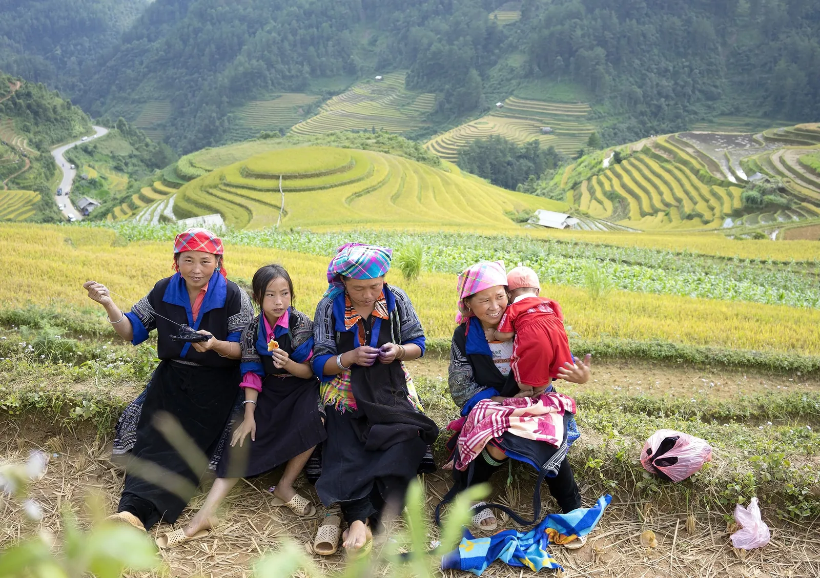 Phụ nữ và trẻ em người Mông mặc trang phục truyền thống ngồi bên ruộng bậc thang vàng ở Mù Cang Chải.