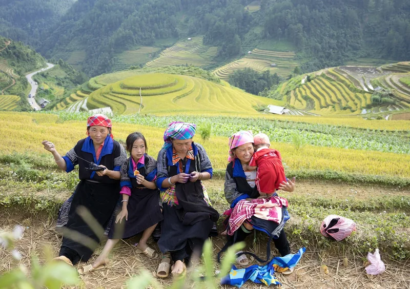 Phụ nữ và trẻ em người Mông mặc trang phục truyền thống ngồi bên ruộng bậc thang vàng ở Mù Cang Chải.