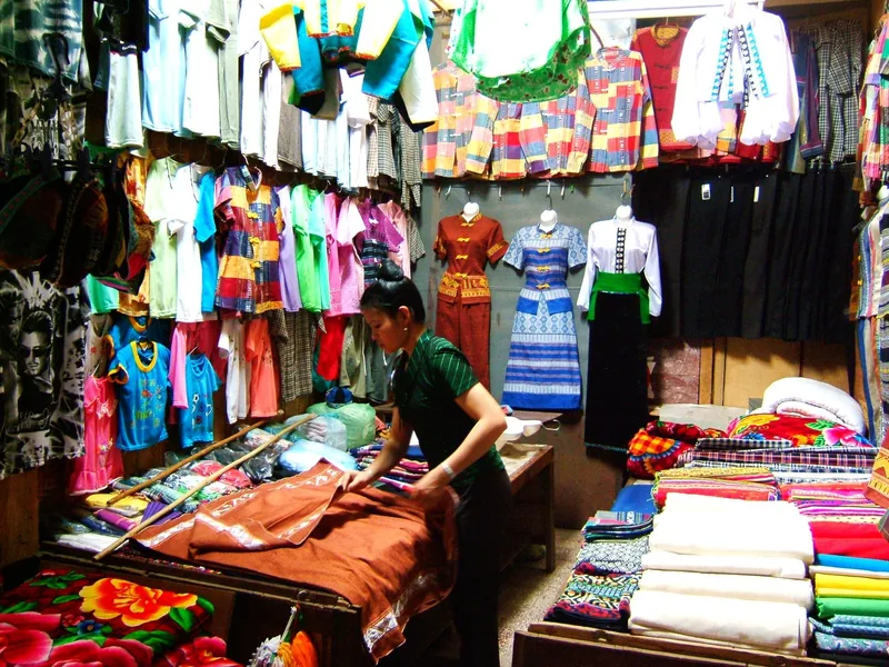 Người bán hàng xếp vải và trang phục truyền thống sặc sỡ trong gian hàng đông đúc ở chợ Mường Lò, Nghĩa Lộ.