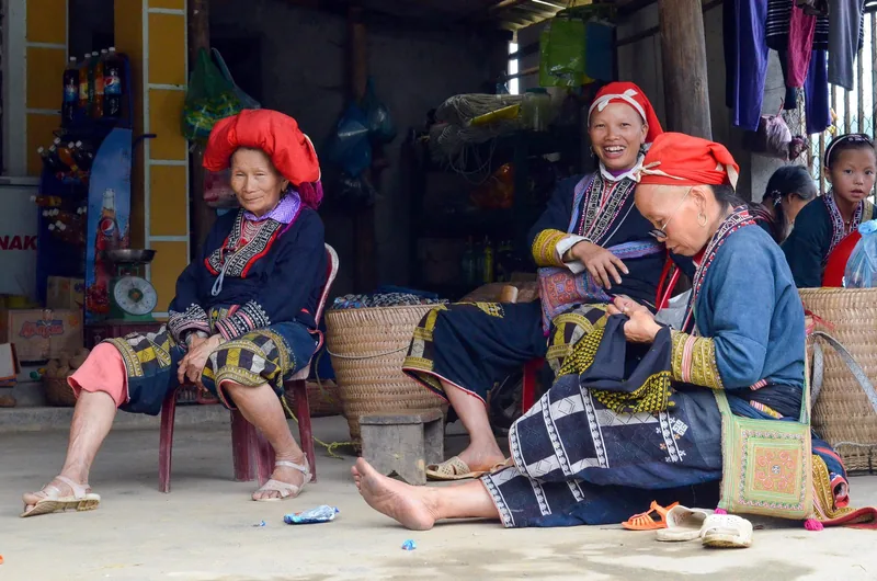 Phụ nữ Dao Đỏ với khăn đỏ và trang phục thêu ngồi trò chuyện trước một cửa hàng ở Sapa.